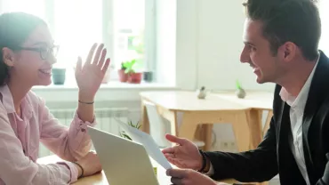 Dos personas sonríen mientras conversan en una oficina luminosa.