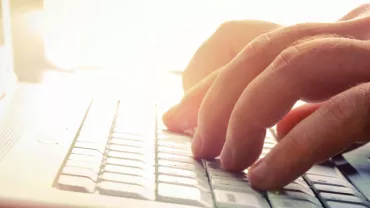 Manos escribiendo en un teclado de computadora portátil con luz de fondo.