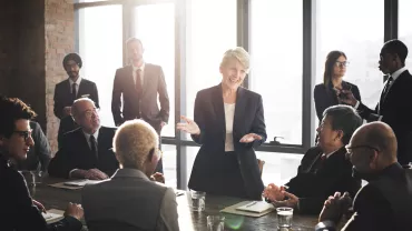 Mujer presentando en reunión de negocios con colegas atentos.