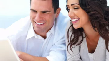 Pareja sonriendo mientras usa una computadora portátil.