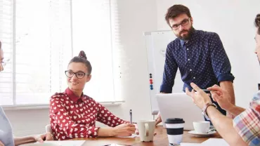 Cuatro personas trabajando en equipo en una reunión alrededor de una mesa.