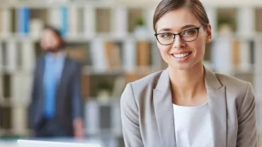 Mujer sonriente con gafas en una oficina moderna.