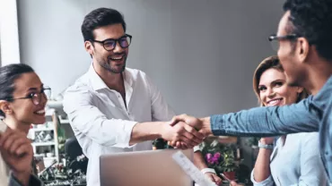 Personas en una reunión sonríen y se dan la mano.
