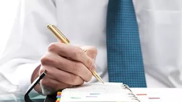 Hombre con camisa blanca y corbata azul escribiendo en un cuaderno.