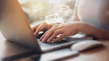 Persona escribiendo en portátil, iconos de correo flotando.
