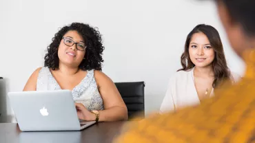 Dos mujeres en una reunión, una usando laptop.