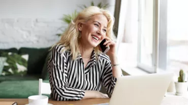 Mujer sonriendo y hablando por teléfono mientras trabaja en una laptop.