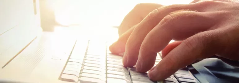 Manos escribiendo en un teclado de computadora portátil con luz de fondo.