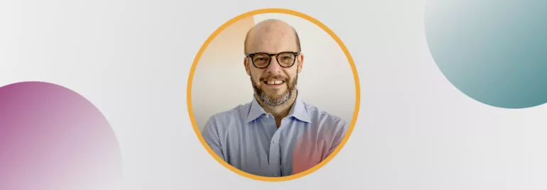 Retrato de un hombre calvo con barba, usando gafas, en un marco redondo.