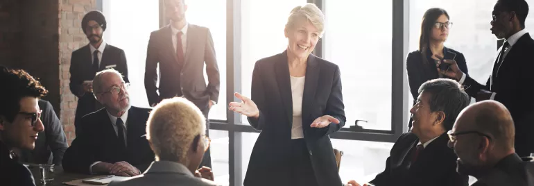 Mujer presentando en reunión de negocios con colegas atentos.