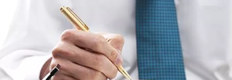 Hombre con camisa blanca y corbata azul escribiendo en un cuaderno.