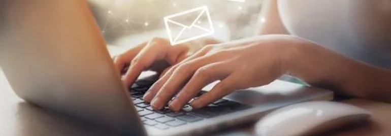 Persona escribiendo en portátil, iconos de correo flotando.