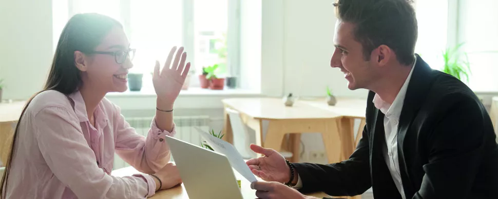 Dos personas sonríen mientras conversan en una oficina luminosa.