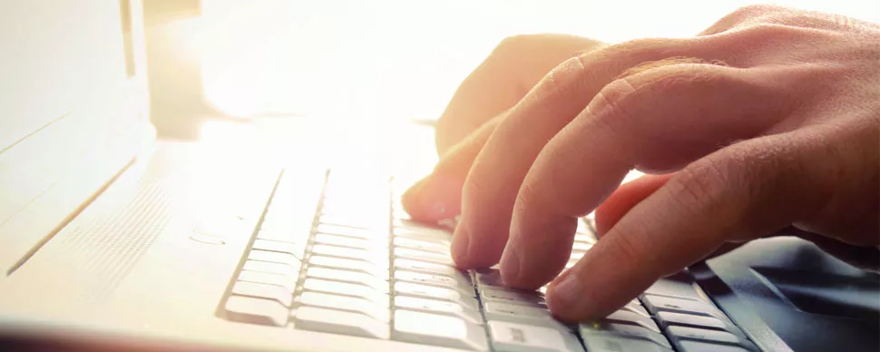 Manos escribiendo en un teclado de computadora portátil con luz de fondo.
