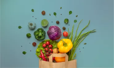 Bolsa con verduras frescas, incluyendo pimiento amarillo y col morada, sobre fondo azul.