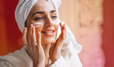Mujer aplicando crema facial con una toalla en la cabeza.