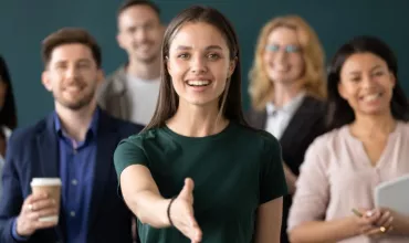 Mujer sonriente saluda con la mano extendida, rodeada de personas.