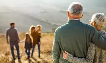 Pareja mayor mirando a una familia con niños en un campo.
