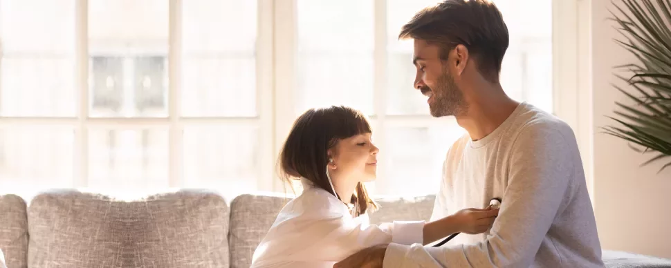 Niña jugando al doctor con su padre en la sala de estar.