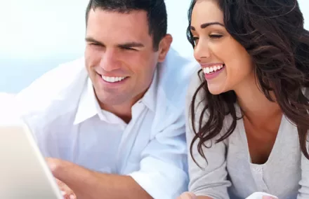 Pareja sonriendo mientras usa una computadora portátil.