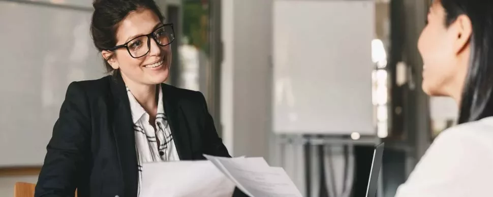 Dos mujeres conversan en un entorno de oficina, una toma notas.