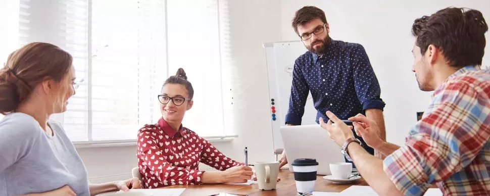 Cuatro personas trabajando en equipo en una reunión alrededor de una mesa.