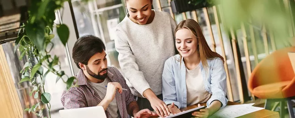 Tres personas colaboran en un proyecto en una mesa, una sobre una laptop.