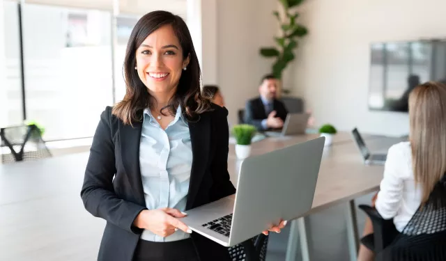 Mujer con laptop sonriendo en sala de reuniones.