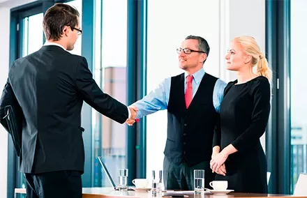 Tres personas en una reunión de negocios, dos dándose la mano.
