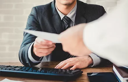 Hombre en traje recibiendo un sobre frente a una computadora.