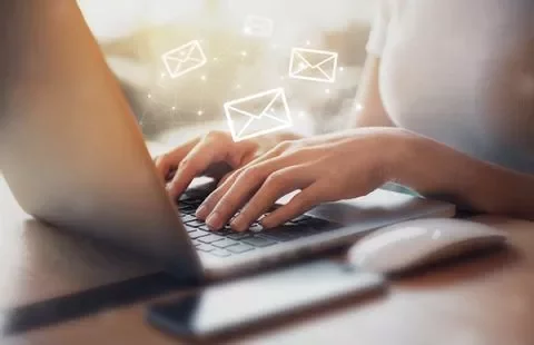 Persona escribiendo en portátil, iconos de correo flotando.