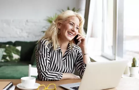 Mujer sonriendo y hablando por teléfono mientras trabaja en una laptop.