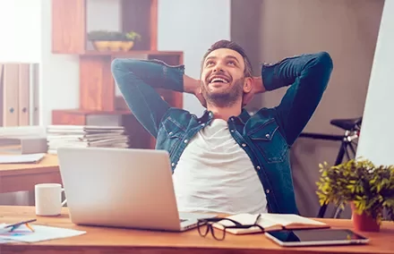 Hombre sonriente relajado en su escritorio con una laptop.